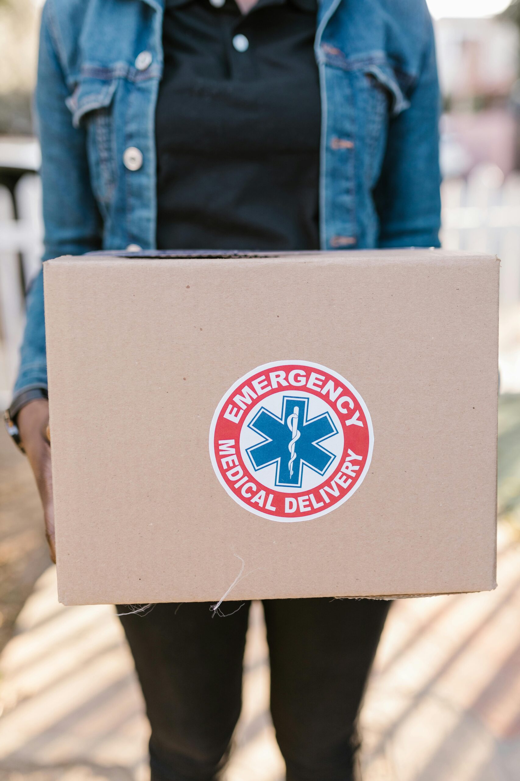 Person holding a box labeled 'Emergency Medical Delivery,' representing urgent healthcare logistics.